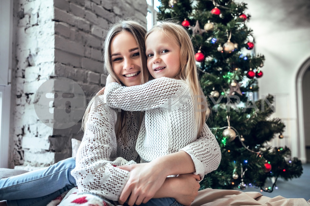 Happy young woman with cute daughter sitting on bed at home