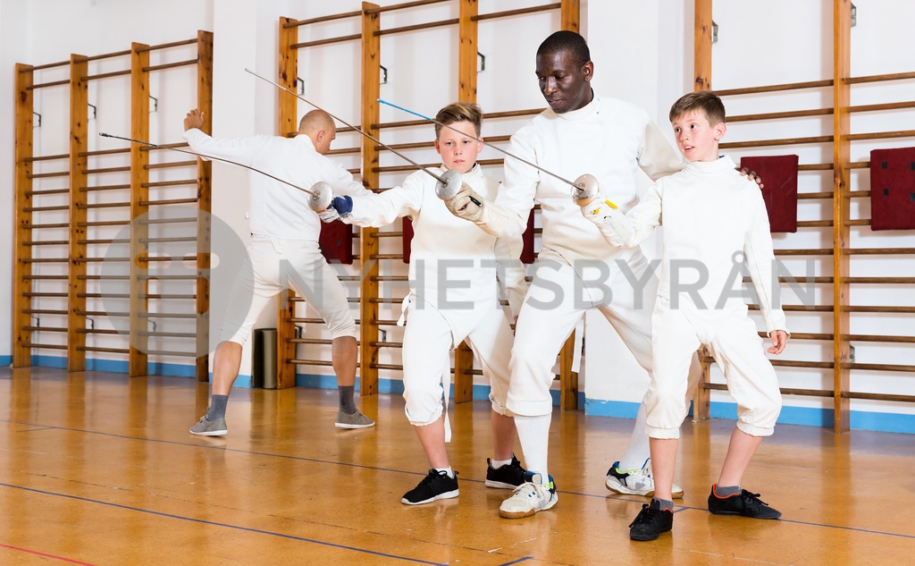 Fencing instructor with young fencers in training room